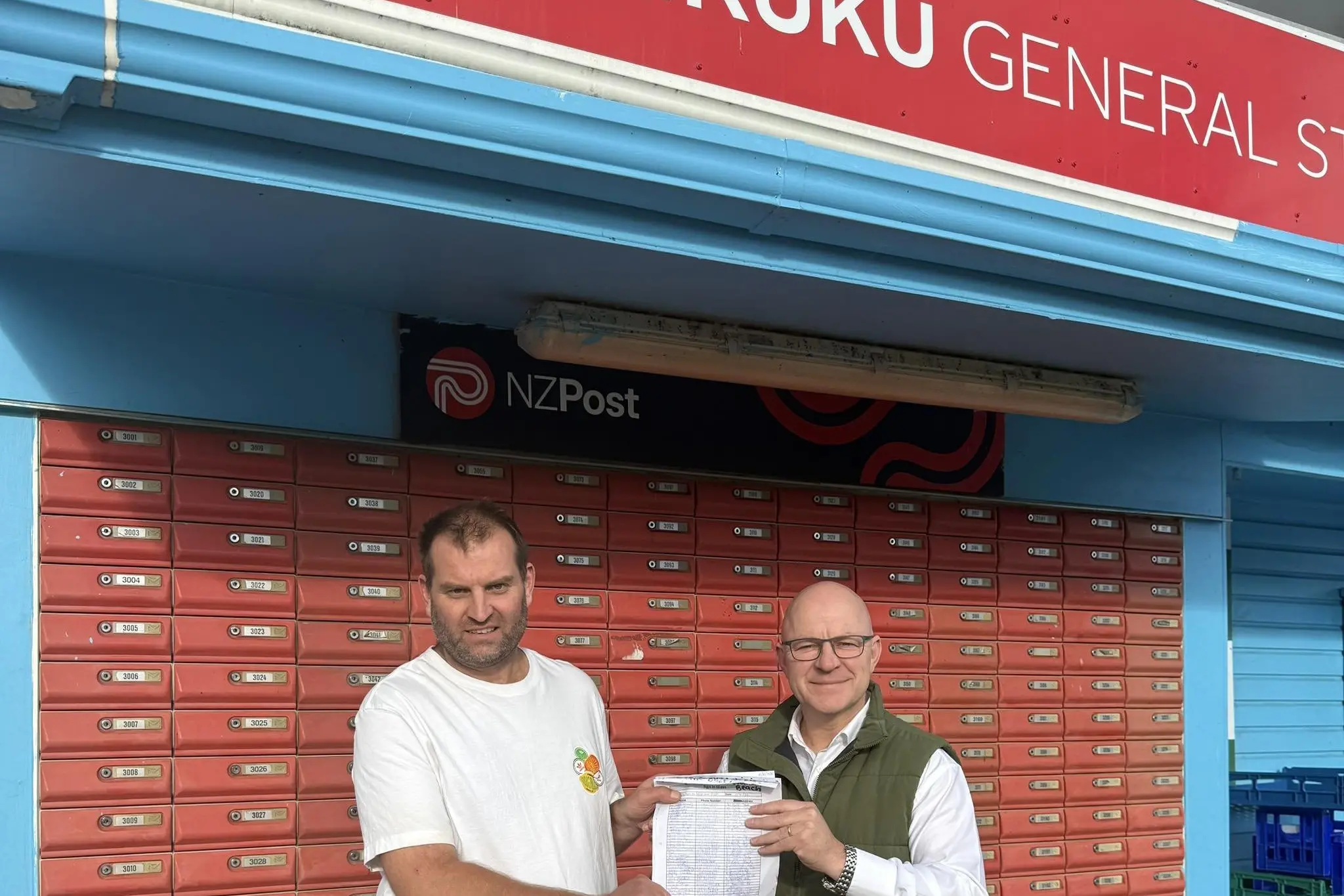 Petition success . . . Joe Kennedy (left) and Matt Doocey with the petition which helped retain postal services in Waikuku Beach. Photo: Supplied