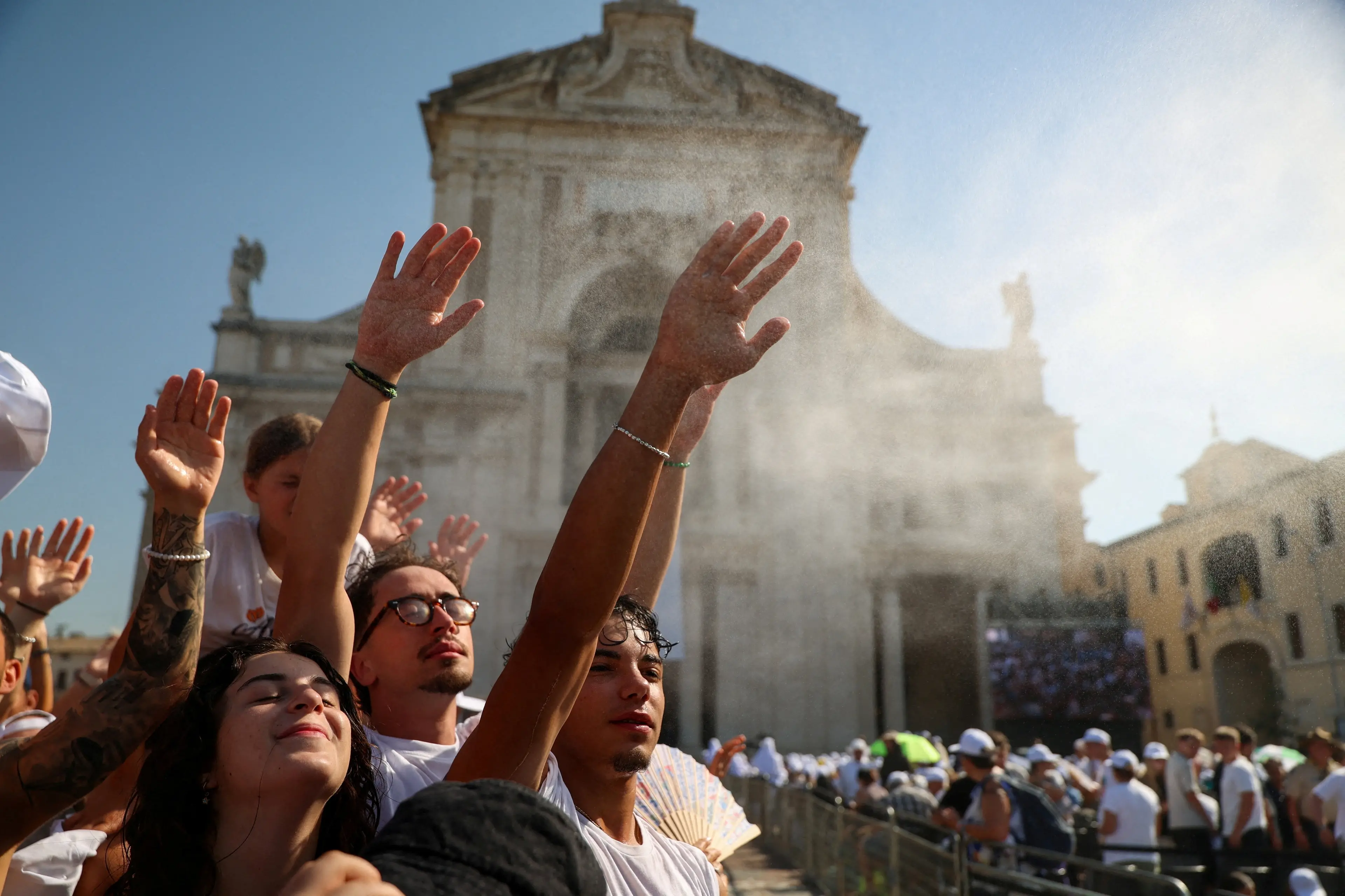 People raise their hands as they cool off in mist outside the Basilica of Santa Maria degli Angeli while gathering for Pope Leo\\u2019s visit marking the 800th anniversary of the death of St. Francis, during a heatwave in Assisi, Italy. Photo: Reuters