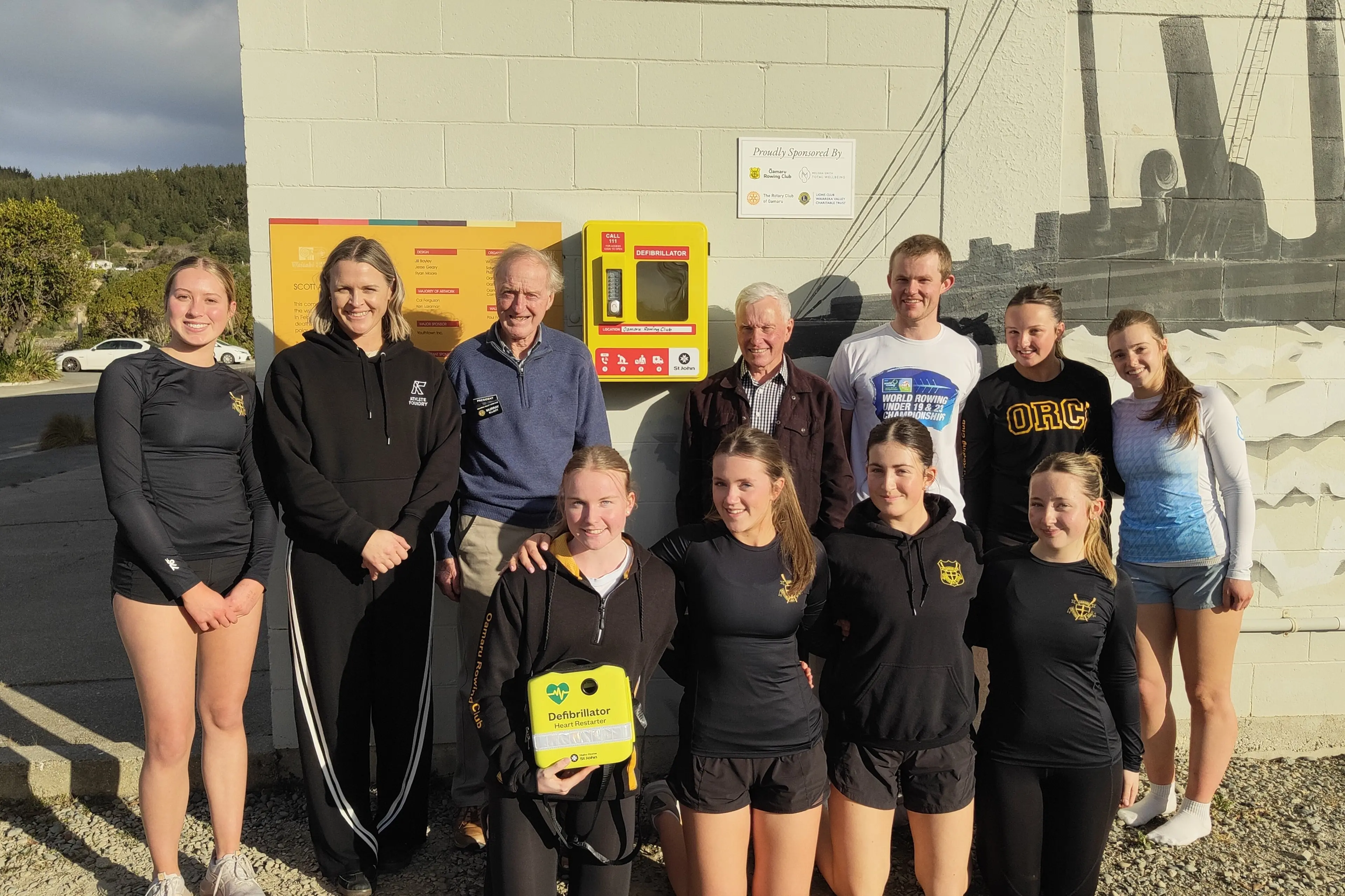 The community behind the installation of the defibrillator at the Oamaru Rowing Club. (Left to right) back row: Kaiah Rawson, Melissa Smith (Total Wellbeing), Murray Elliott (president Wairareka Valley Lions Club), Miles Koberstien (Rotary Club of Oamaru), Logan Docherty (Oamaru Rowing Club coach), Anabel King, Milly Paterson. Front row: Bridget Spittle, Evie Mitchell, Bailey Pearson, Charlie Burnett. Photo: Supplied.
