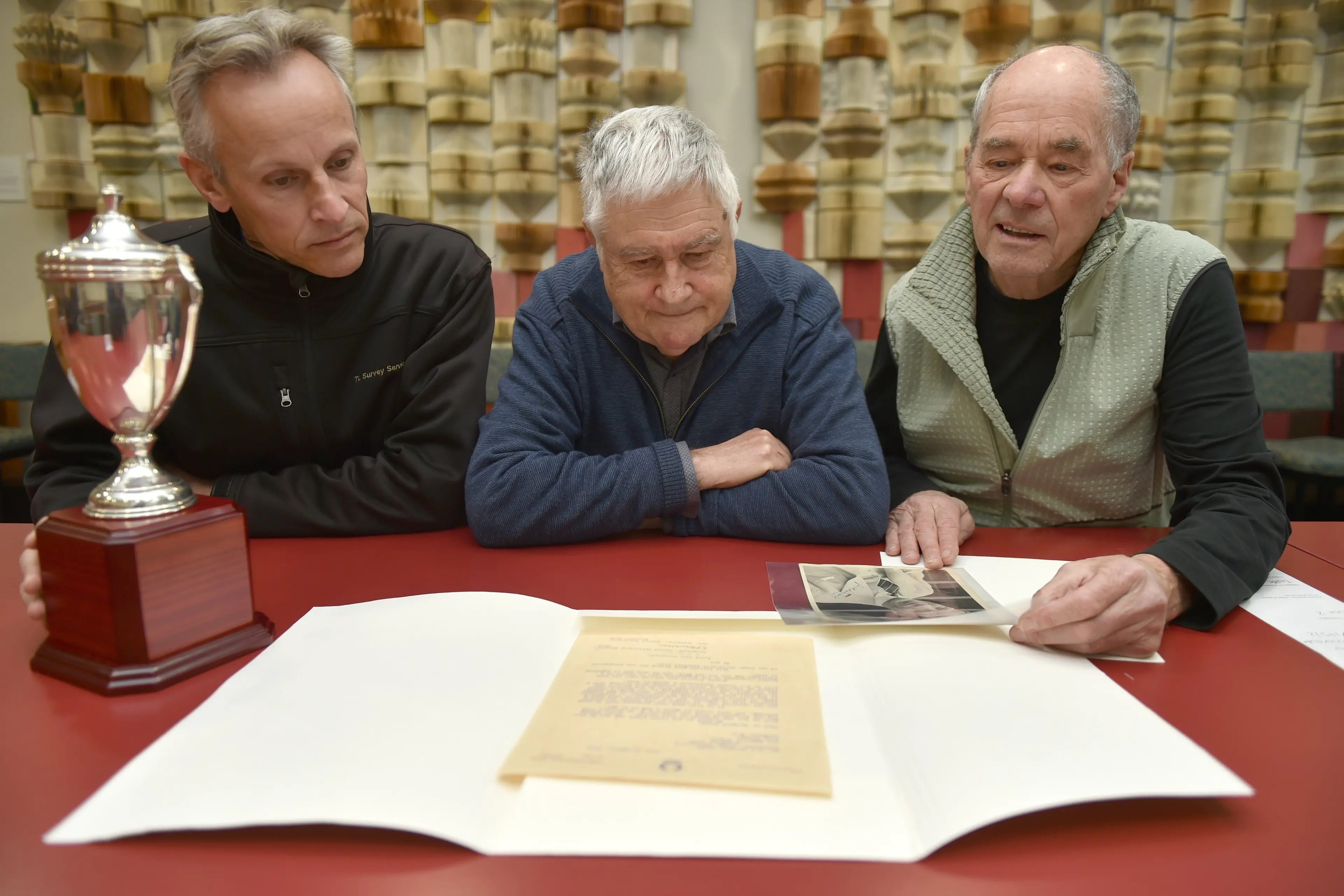 Hill City-University president Mark Geddes, life member Bruce Beath and patron Lindsey Dey look over records of the Lovelock One Mile Challenge Cup at the Hocken Library. Photo: Gregor Richardson