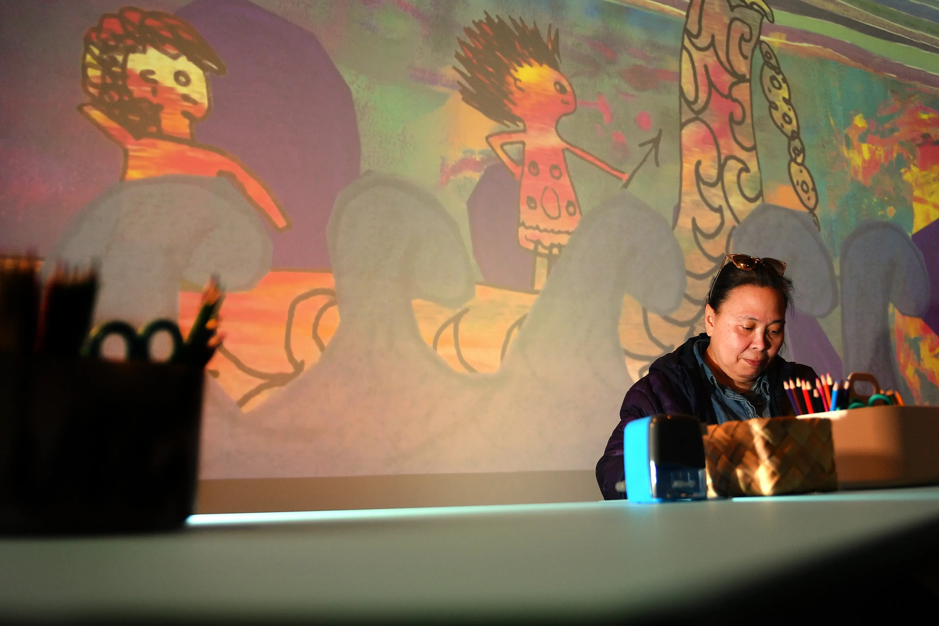 Dunedin artist Fides works on a piece while art is projected on to a T\\u016Bhura Otago Museum wall in the background. Photo: Stephen Jaquiery