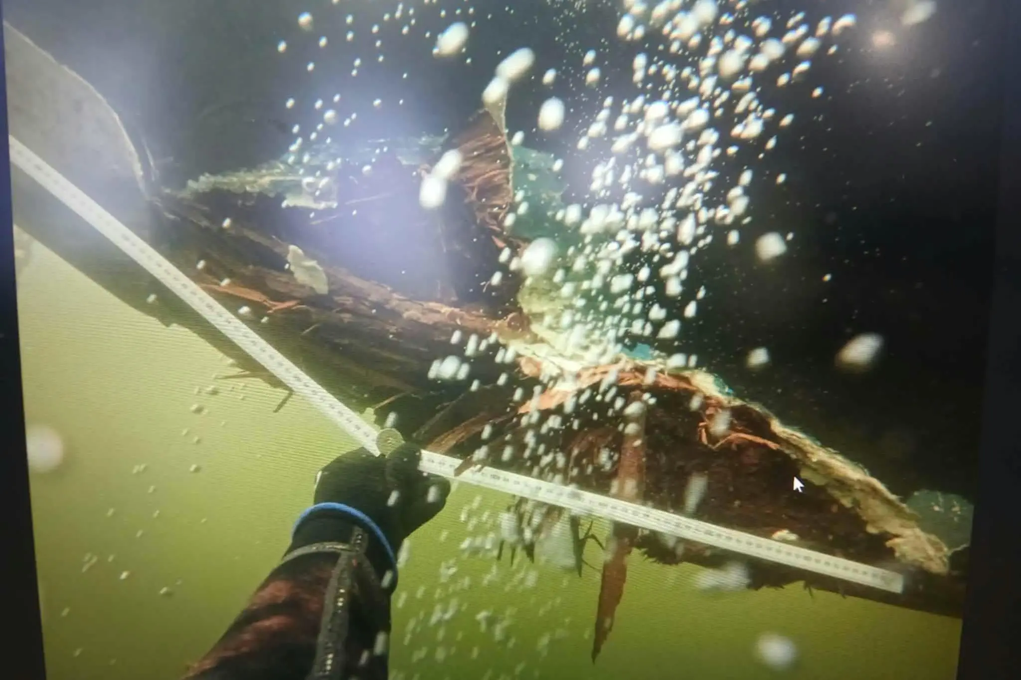A diver holds a ruler up in front of damage apparently to the hull of the Heritage Explorer. Photo: Supplied