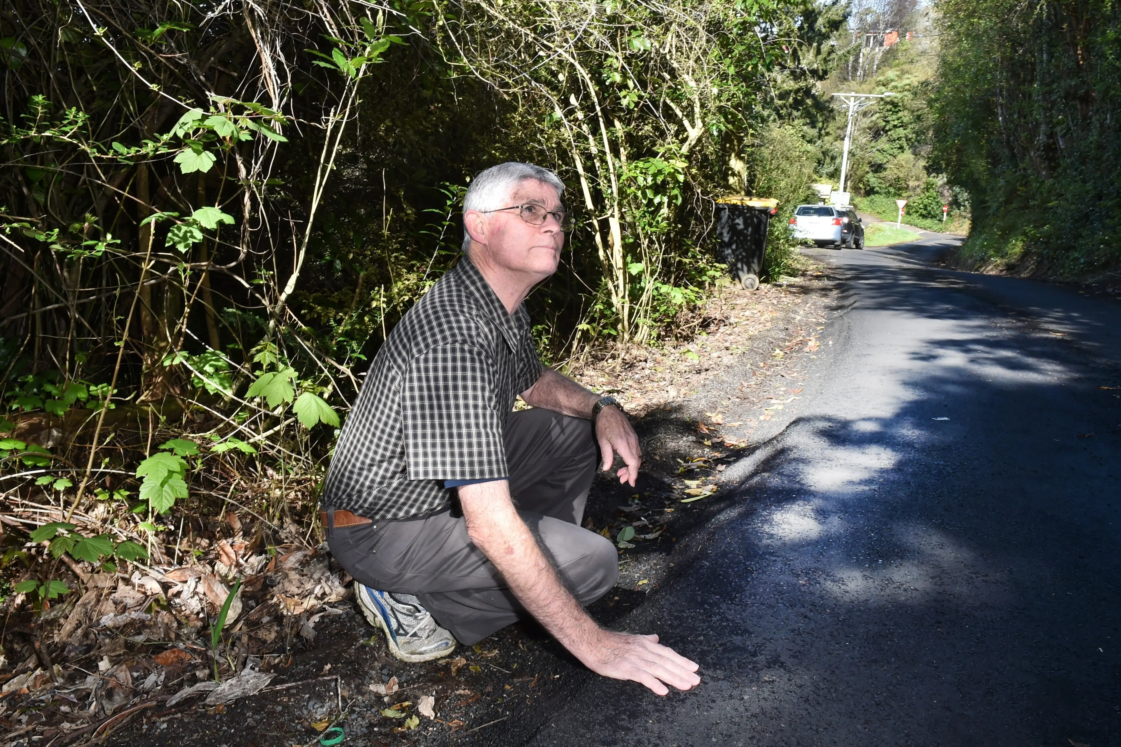 John Lydiate is concerned about a significant slump in Tanner Rd near Ross Creek. The ground immediately behind him is being held up by a retaining wall. Photo: Gregor Richardson