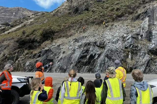 Pupils from Makarora School watch rock scaling work being done on SH6. Photo: NZTA