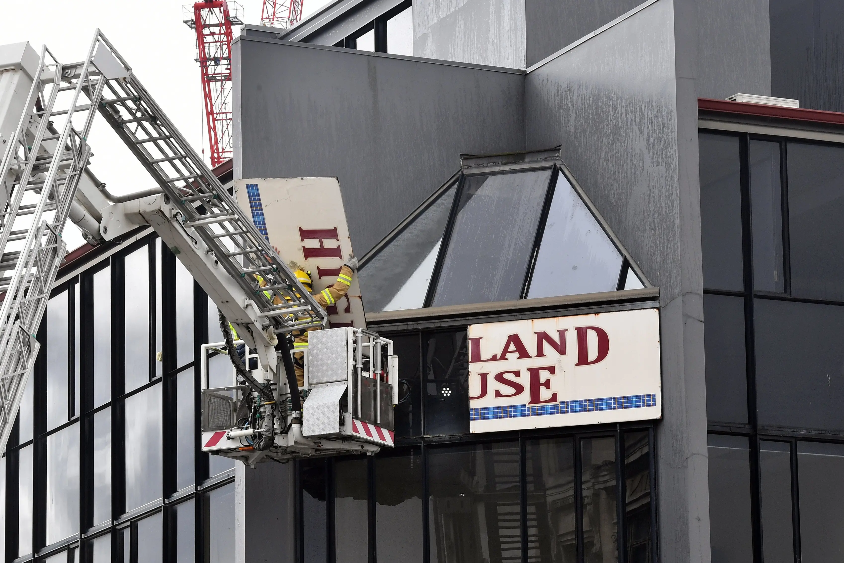 Firefighters use a boom lift to remove part of the \"Highland House\" sign from a building in Moray Pl. Photo: Stephen Jaquiery