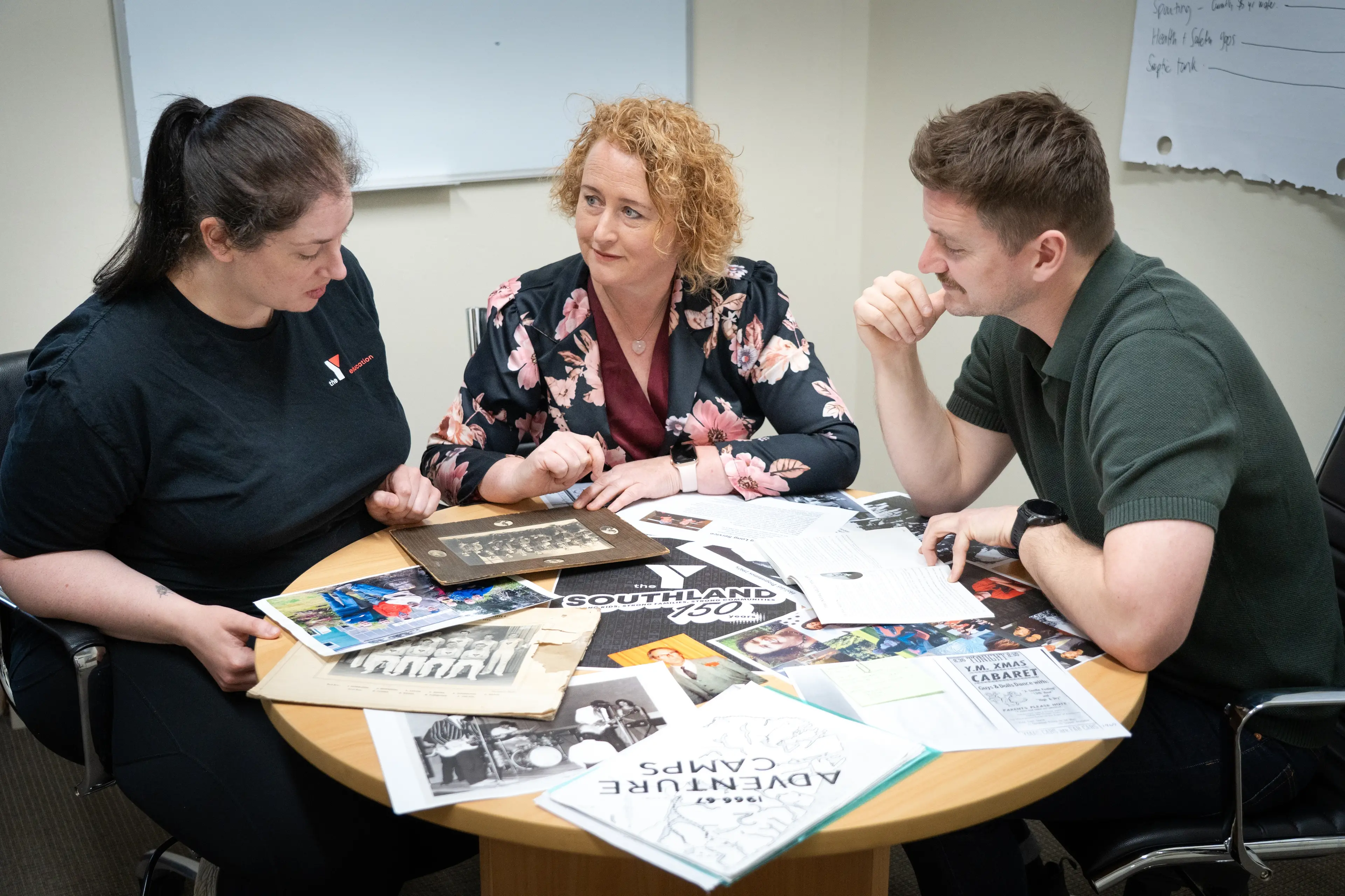 Sorting through the photographs they received for The Y 150 anniversary exhibition are (from left) education tutor Caitlin Barrie, executive assistant Helen Hart, and chief executive officer Steve Broad. Photo: Supplied.