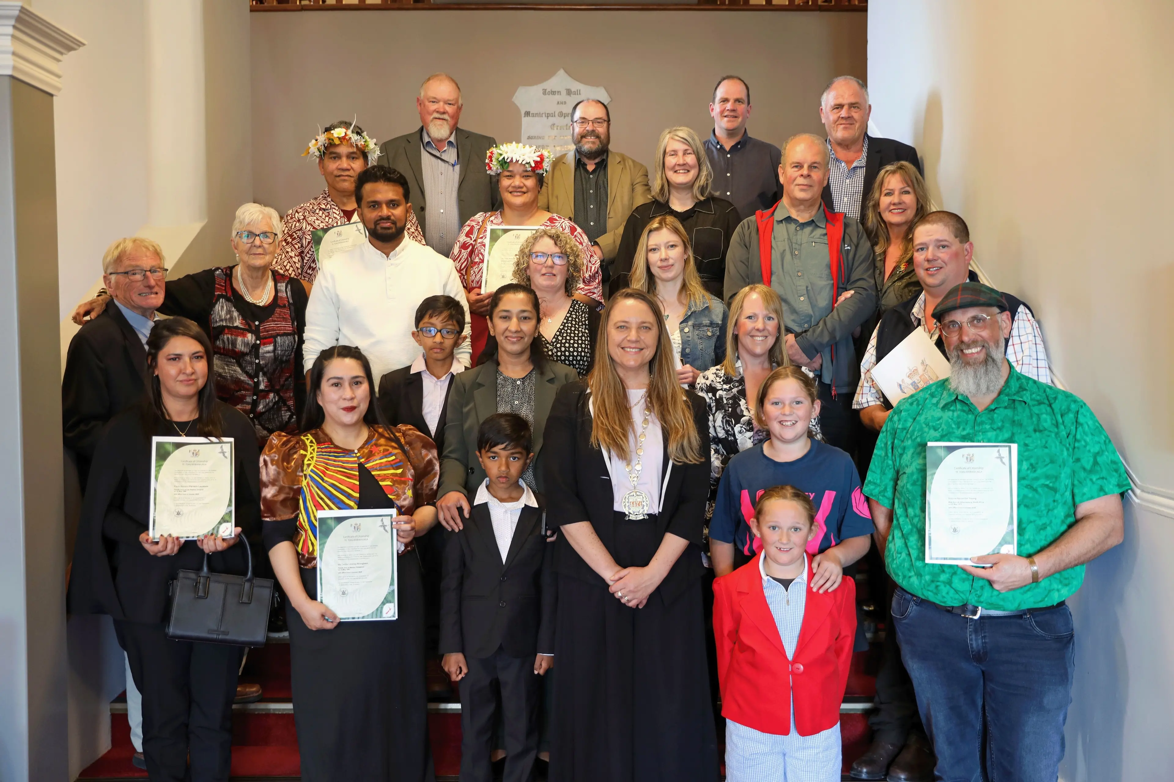 The 20 new citizens who were recently sworn in at a ceremony at the Oamaru Opera House proudly present their citizenship certificates alongside Waitaki Mayor Mel Tavendale [front centre] and Crs Frans Schlack, Dan Lewis, Jeremy Holding and John McCone, in the back row. Photo: Waitaki District Council