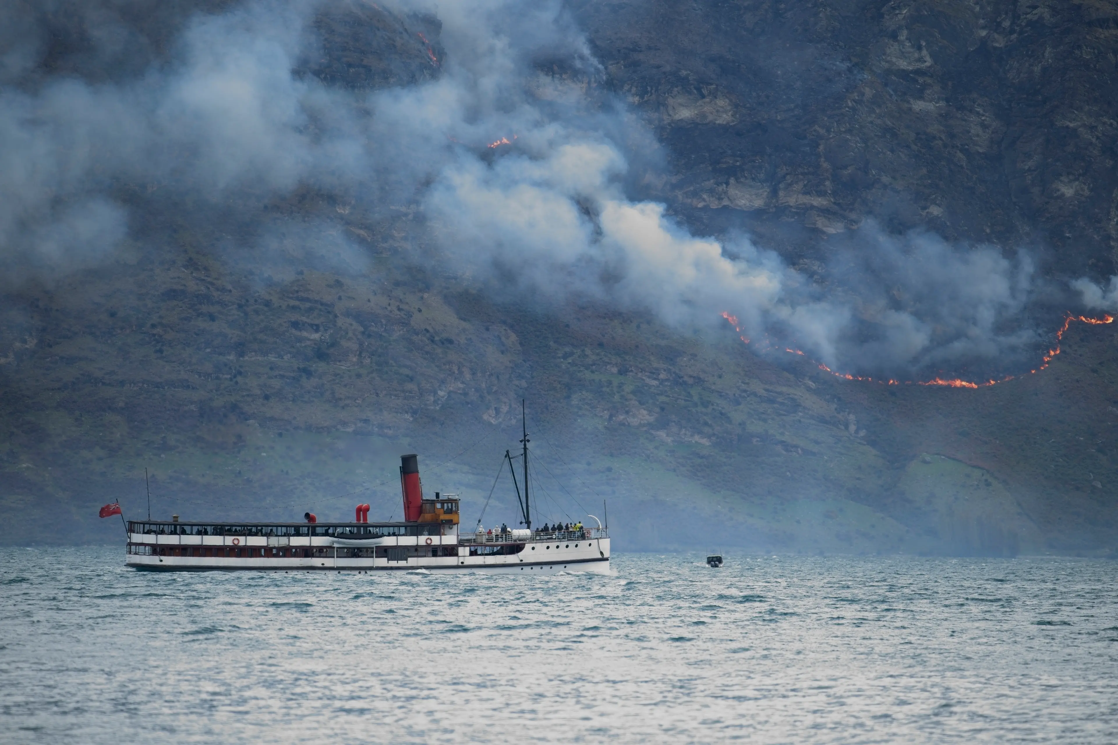 Fiery backdrop: RealNZ\\'s vintage steamship TSS Earnslaw heads across Lake Wakatipu to Walter Peak High Country Farm on Tuesday as a fire burns on the lower slopes of Walter Peak on Tuesday. Photo: Marty Barwood